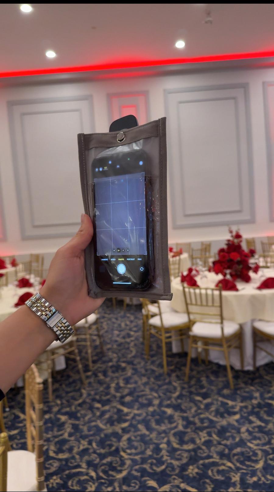 Wedding guest holding a phone in a Notography camera-covering case during a reception