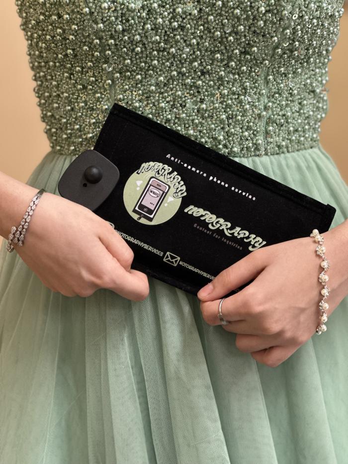 Guest in a sage formal dress holding a Notography anti-camera phone case